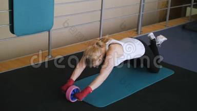 运动垫上的女运动员在健身房做仰卧起坐。 肌肉女运动员用轮子做吸收运动.